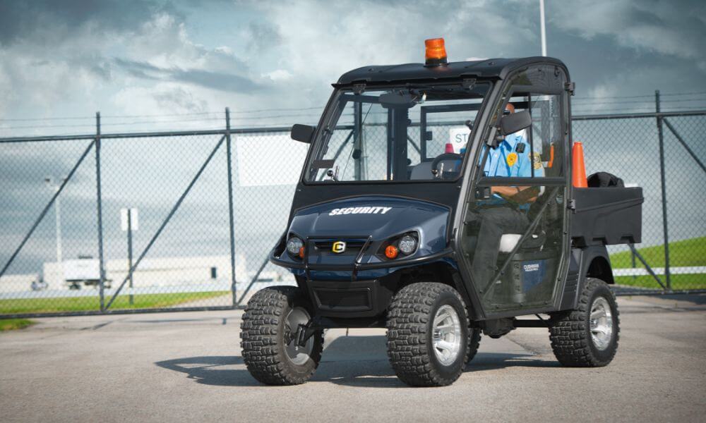 A hand plugs a charger into an E-Z-GO vehicle